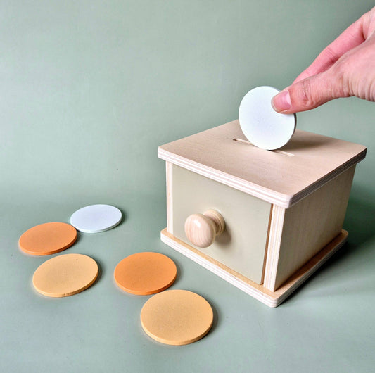 Nahaufnahme: Hand führt eine weiße Scheibe in den Schlitz der Holzbox, orange und gelbe Scheiben liegen daneben.