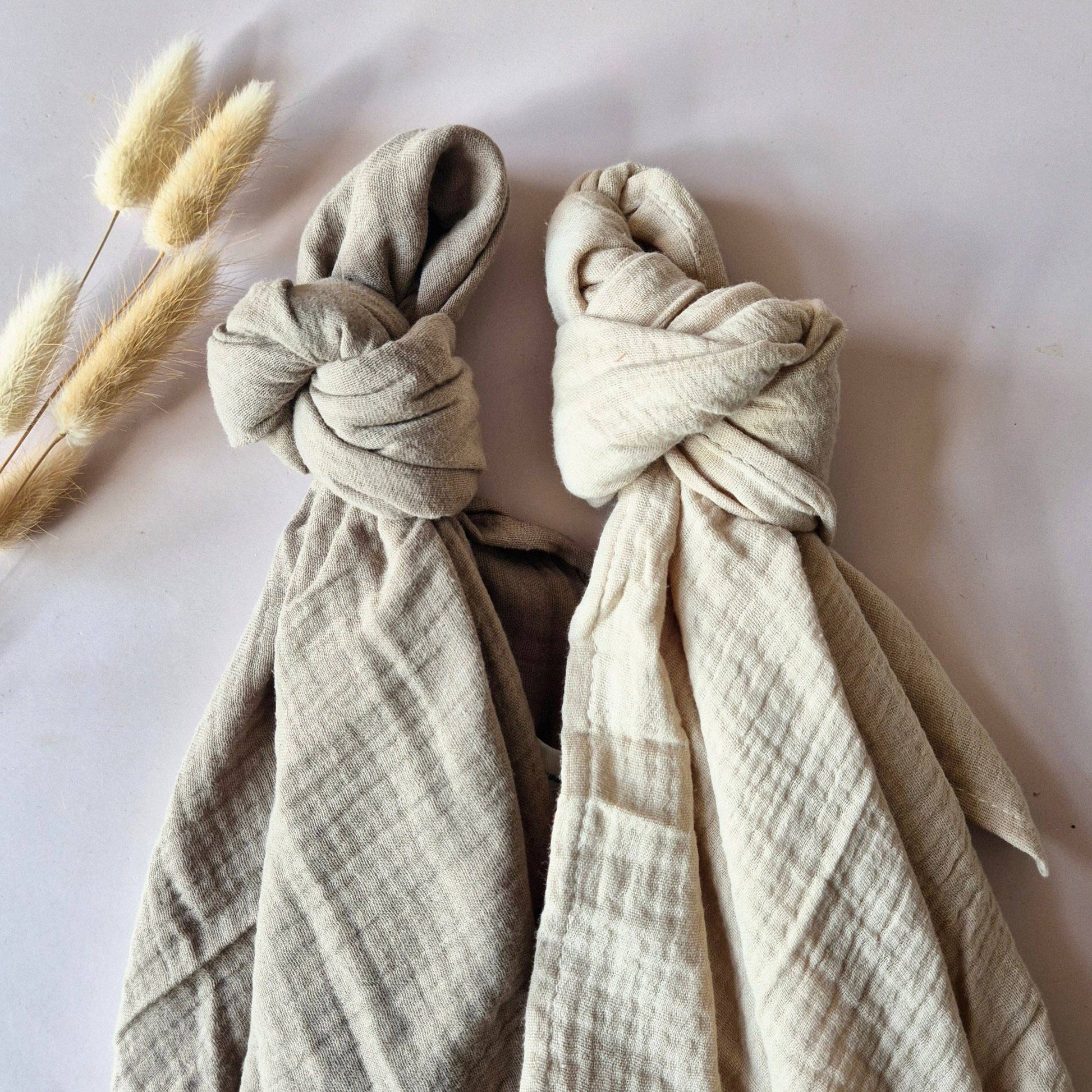 Nahaufnahme zweier verknoteter Mulltücher in Beige und Sand mit Trockenblumen