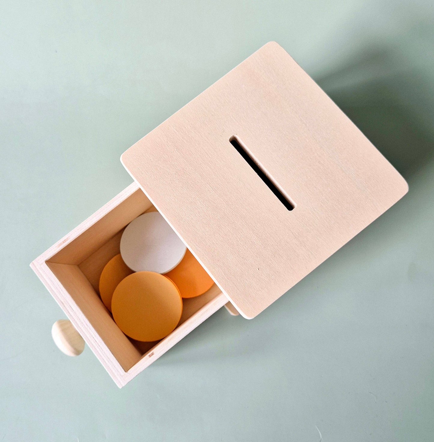 Draufsicht auf die geöffnete Schublade mit gestapelten Scheiben in Weiß, Orange und Gelb in der Holzbox.