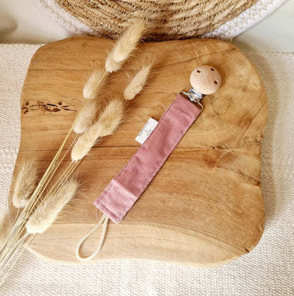 Einzelner Schnullerhalter aus Cord in Puderrosa mit Holzclip auf Holzbrett mit Trockengras