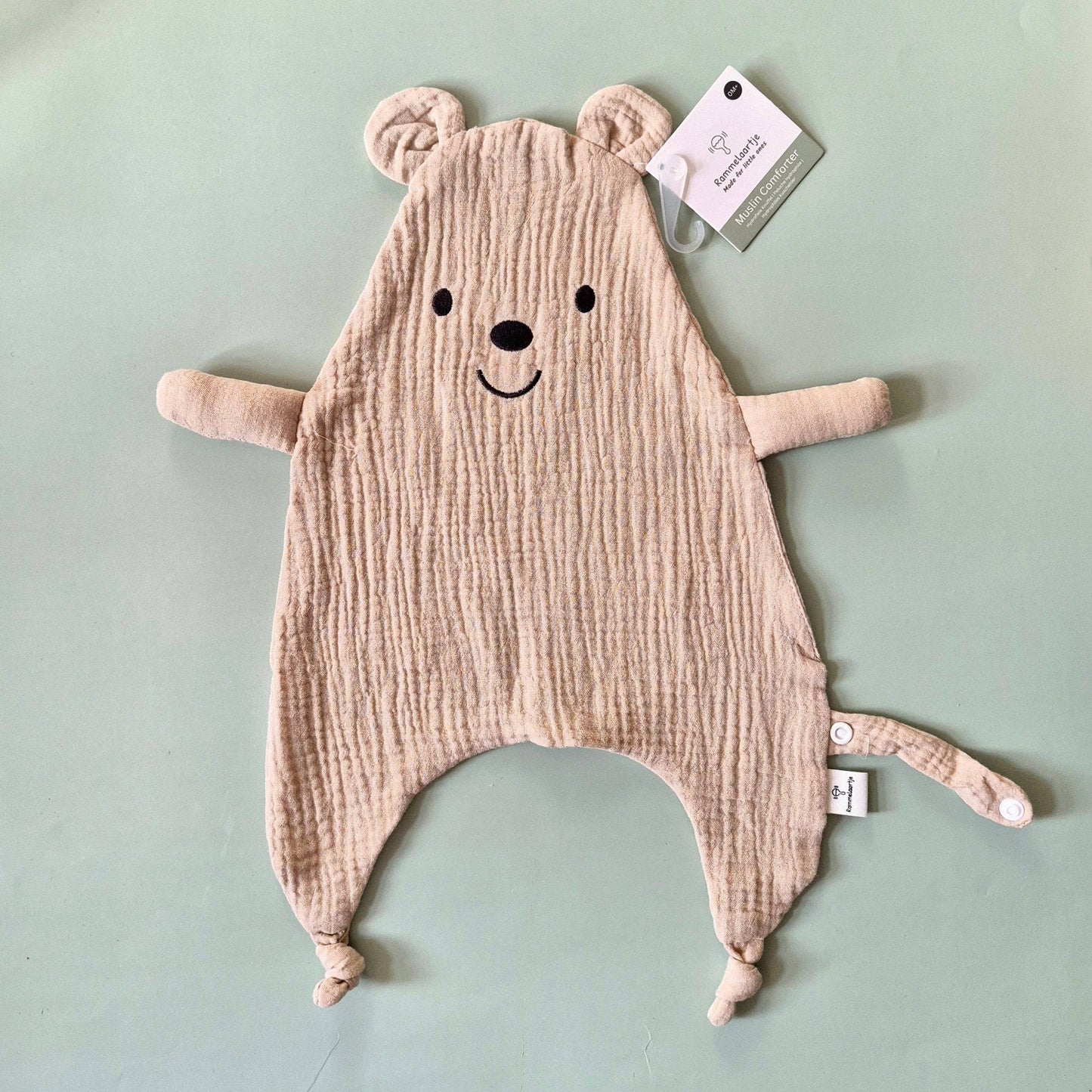 Musselin Kuscheltuch Bär in Beige mit Knoten an den Füßen und Schlaufe auf hellem Untergrund.
