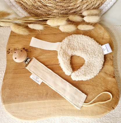 Schnullerhalter in Beige mit cremefarbenem Bouclé-Greifring und Holzclip auf Holzbrett