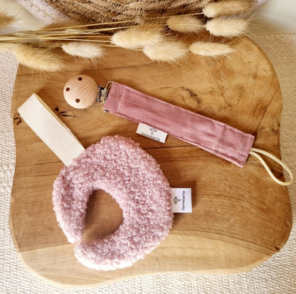 Schnullerhalter in Puderrosa mit rosa Bouclé-Greifring und Holzclip auf hellem Holzbrett