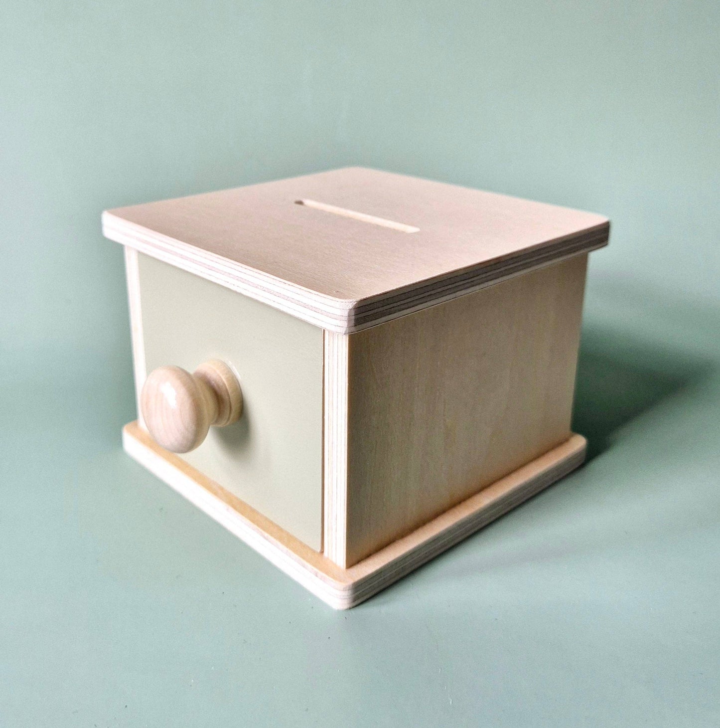 Seitenansicht der geschlossenen Holz-Spielbox mit rundem Holzknauf und Steckschlitz auf grünem Hintergrund.